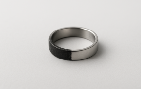 Pierścionek ze stali chirurgicznej leżący na jasnym tle, z wyraźnym kontrastem – połowa powierzchni srebrzysta i błyszcząca, druga połowa przyciemniona i matowa, symbolizująca możliwe czernienie metalu