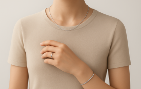 Minimalistyczna wizualizacja 3D przedstawiająca górną część sylwetki osoby w beżowej bluzce, noszącej delikatną biżuterię: cienki srebrny naszyjnik, subtelny pierścionek i prostą bransoletkę na nadgarstku. Tło neutralne, oświetlenie miękkie i studyjne