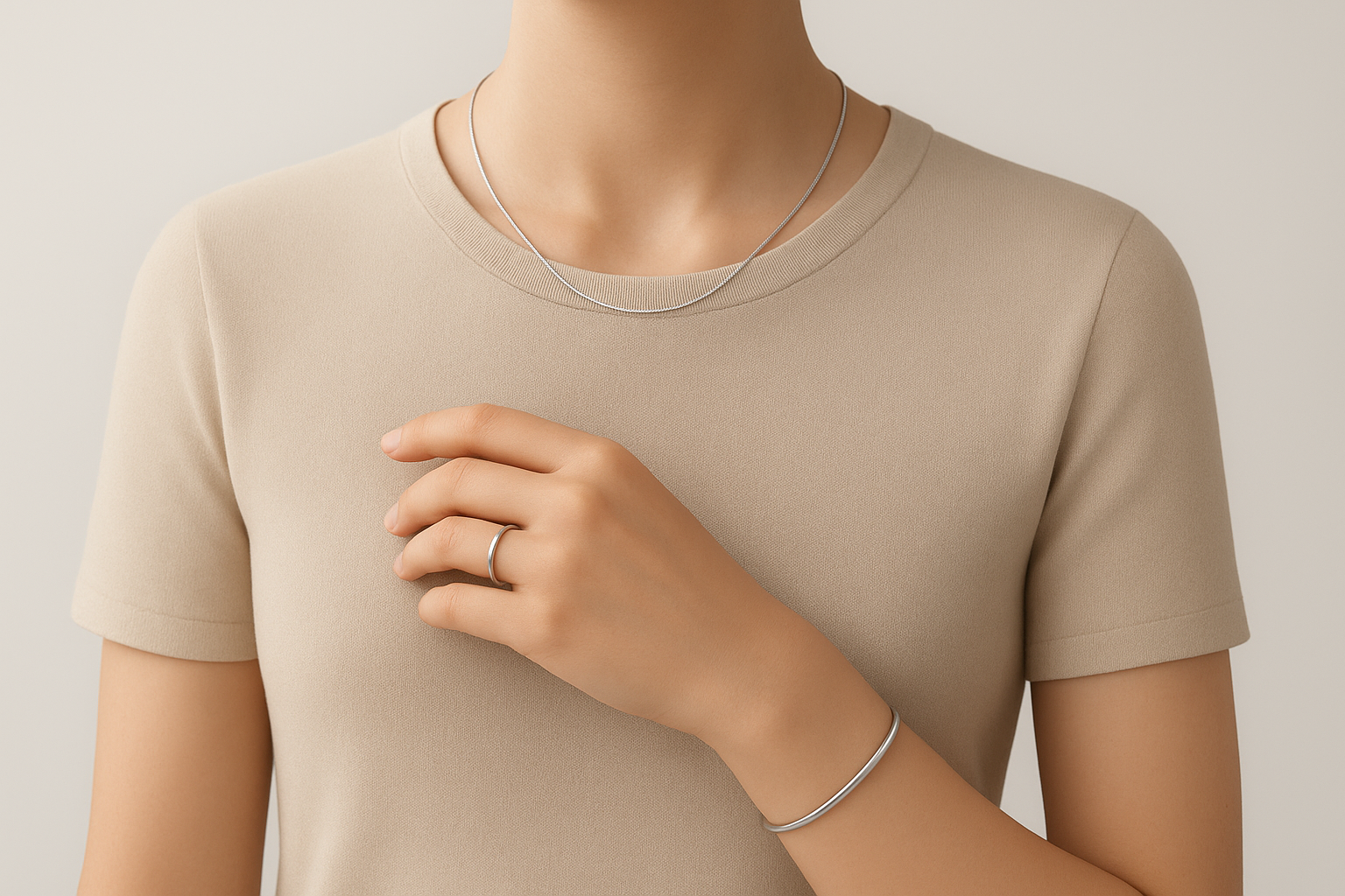 Minimalistyczna wizualizacja 3D przedstawiająca górną część sylwetki osoby w beżowej bluzce, noszącej delikatną biżuterię: cienki srebrny naszyjnik, subtelny pierścionek i prostą bransoletkę na nadgarstku. Tło neutralne, oświetlenie miękkie i studyjne